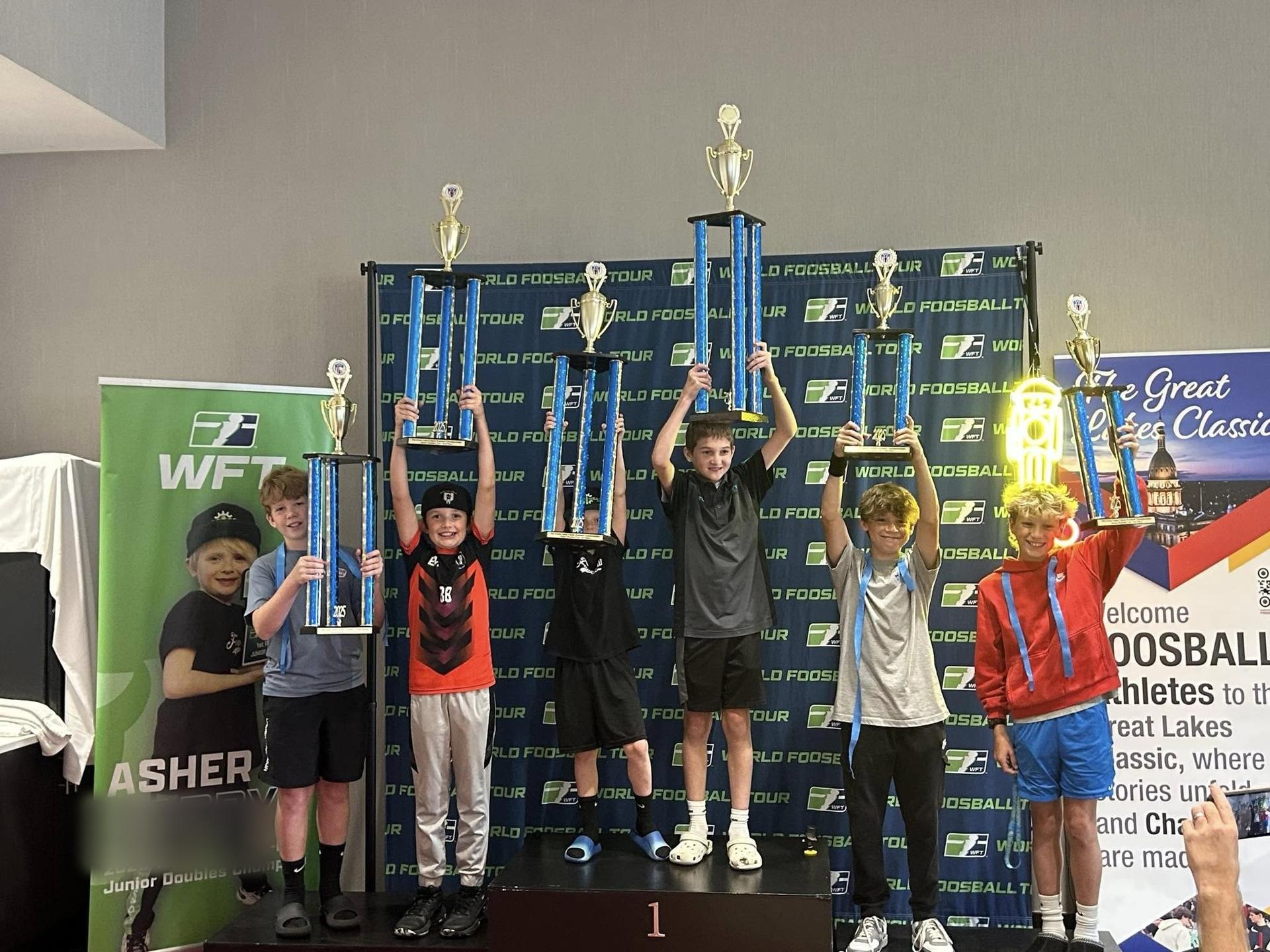 Six young players on the podium lifting championship trophies over their heads at the 2025 Great Lakes Classic