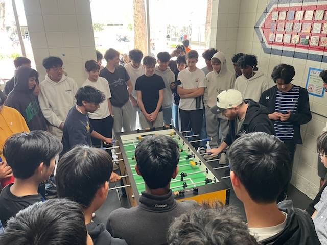 A crowd of high school students around a foosball table at their school club